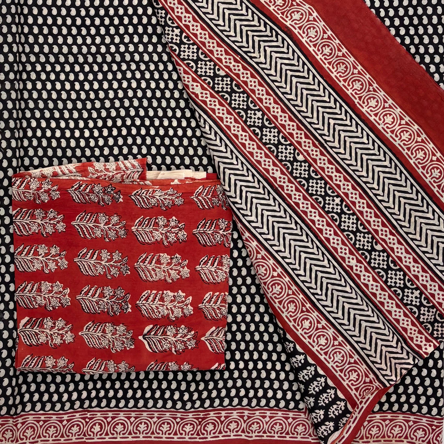 Black base colour cotton saree with all over small beige paisley blockprint, red border and a contrasting red blockprinted blouse material. 