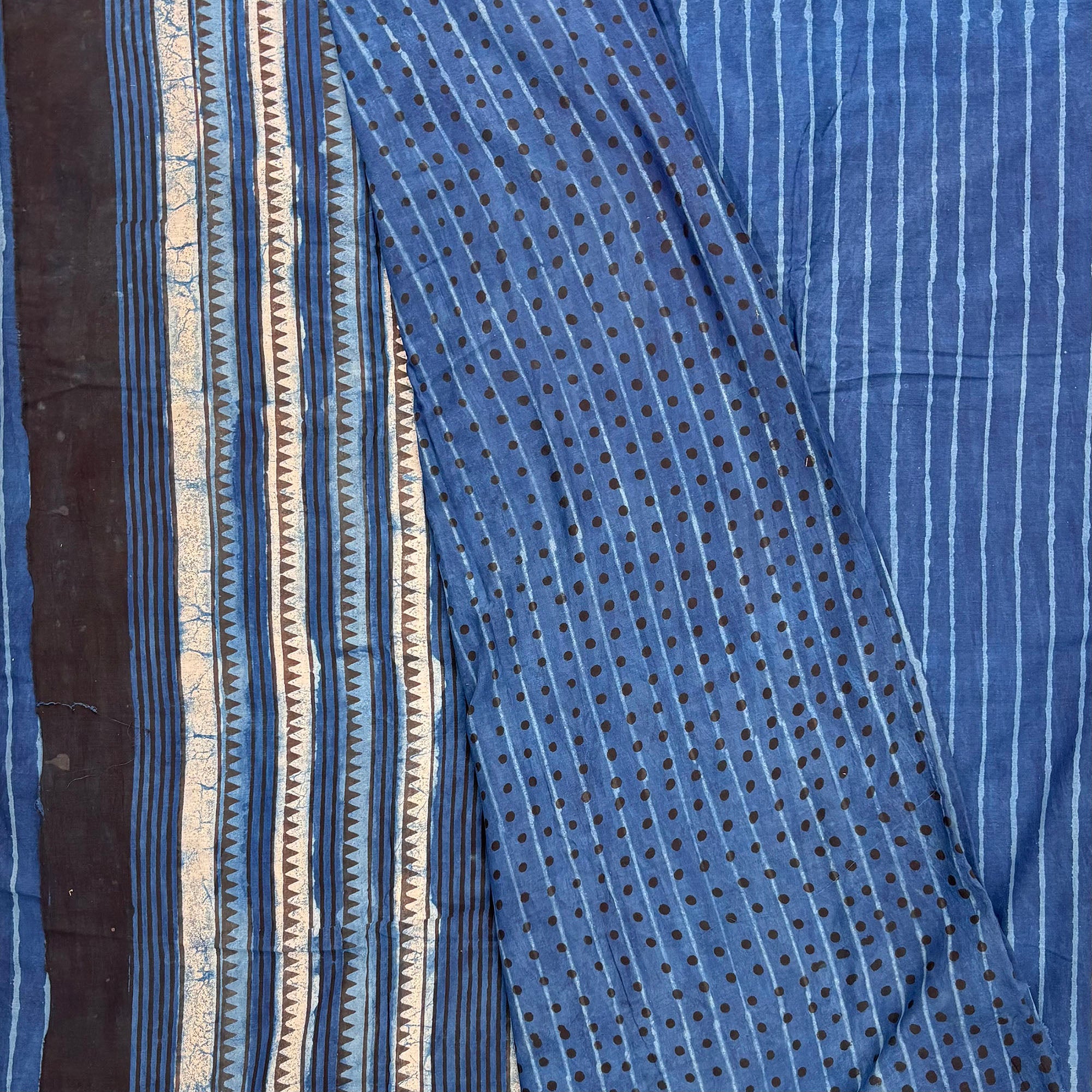 Indigo colour cotton saree with blockprinted stripes on the body and contrasting blouse material with dotted print. Pallu in white black and blue striped pattern.