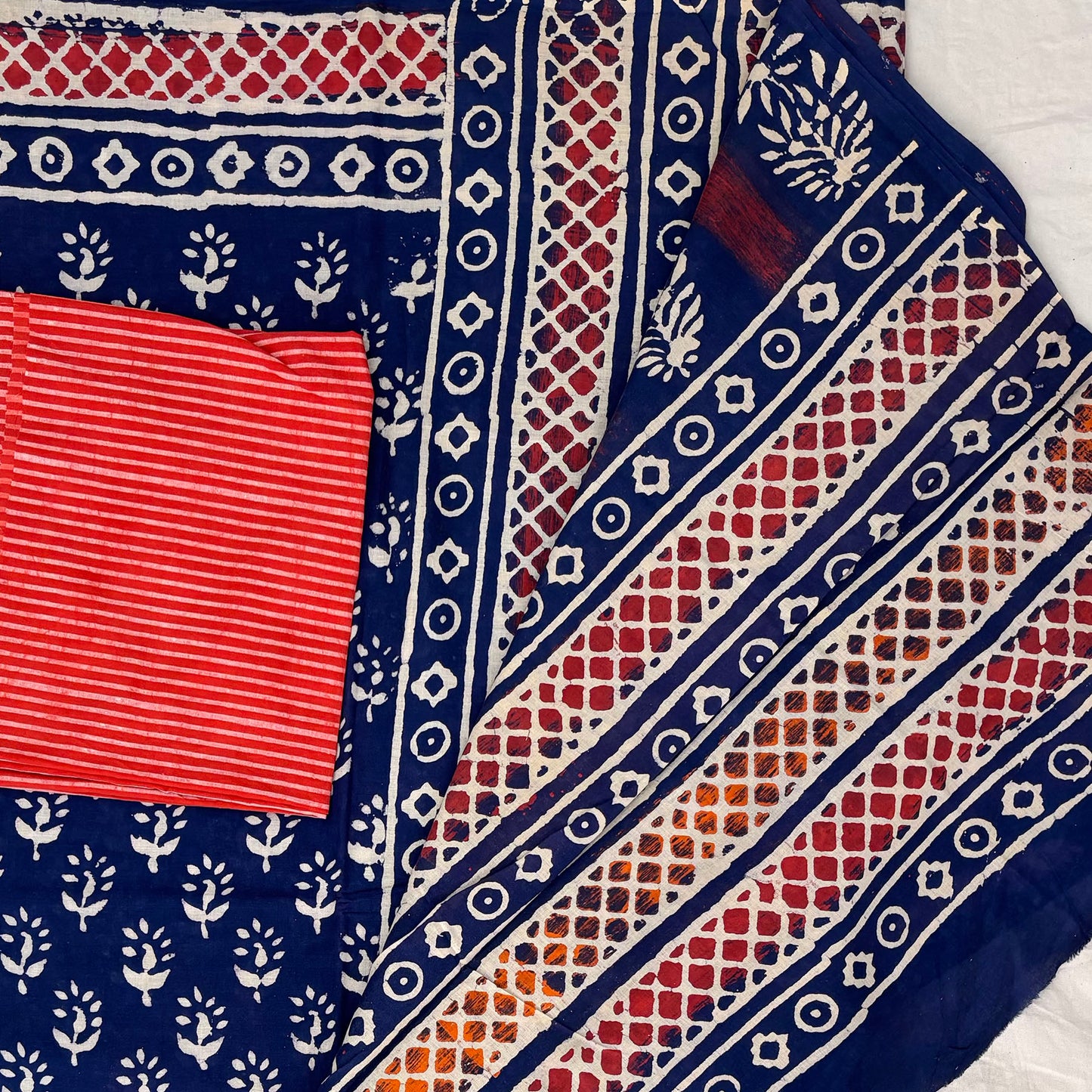Close up of cotton block printed saree with blue base showing pallu and tomato red blouse material.